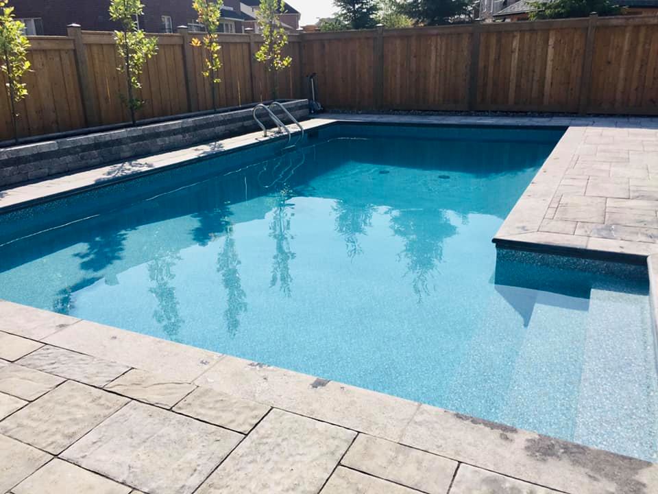 Backyard pool surrounded by custom interlock stone patio and fresh landscaping